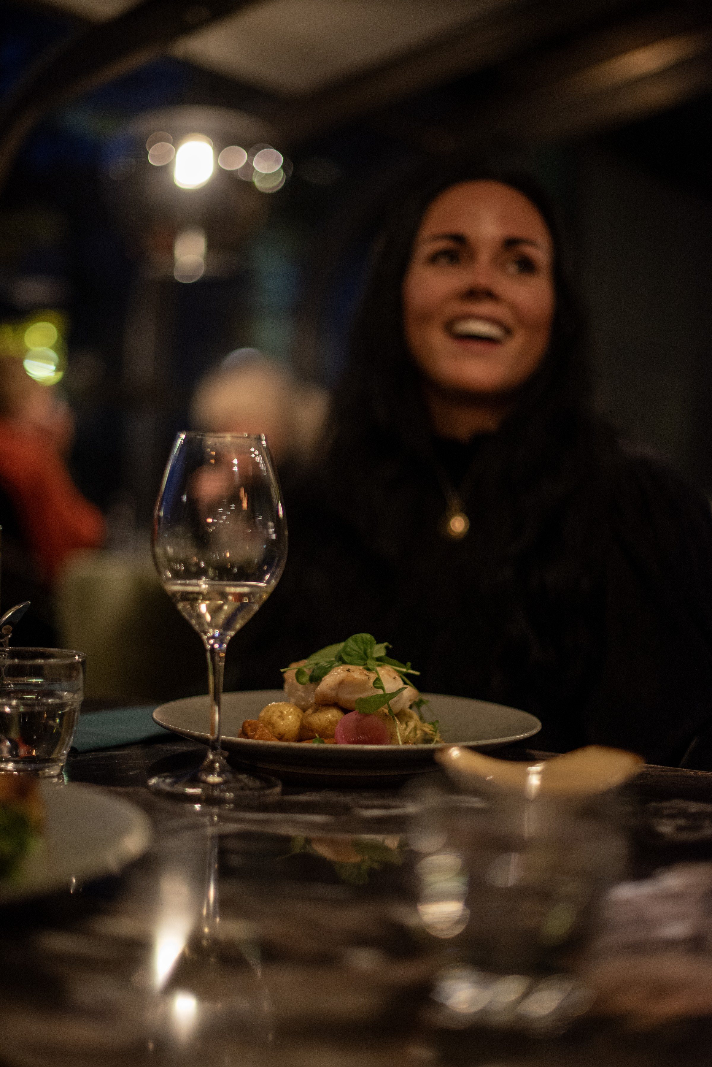 En gjest ler ved bordet en kveld på Strøm, med et glass hvitvin og en tallerken mat foran seg